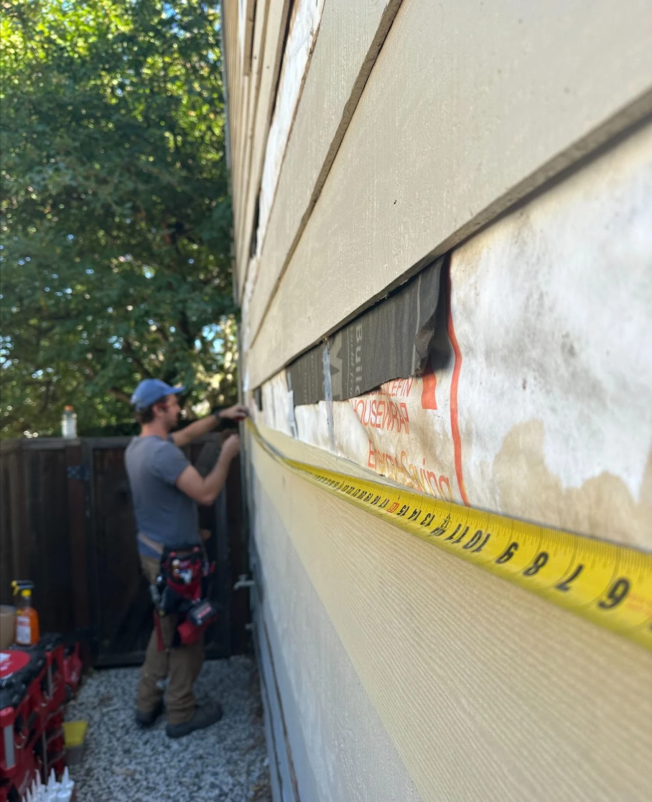 Worker repairing exterior siding with the underlying wall exposed