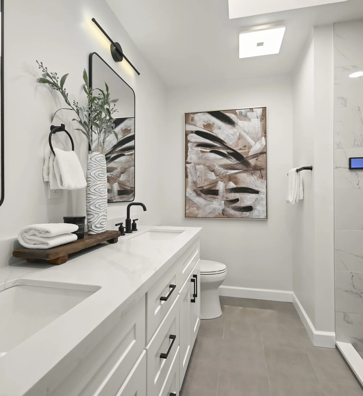 White bathroom vanity with black fixtures beside a tiled shower