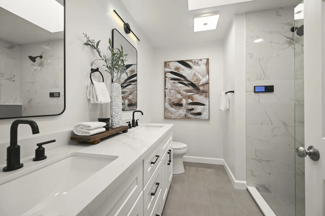 White bathroom vanity with black fixtures beside a glass-enclosed shower