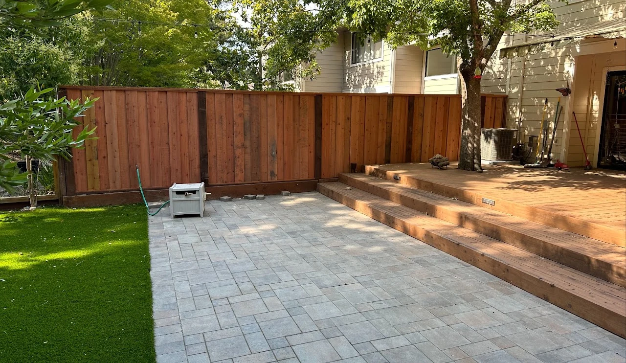 Paver patio beside lawn, wood steps and a privacy fence