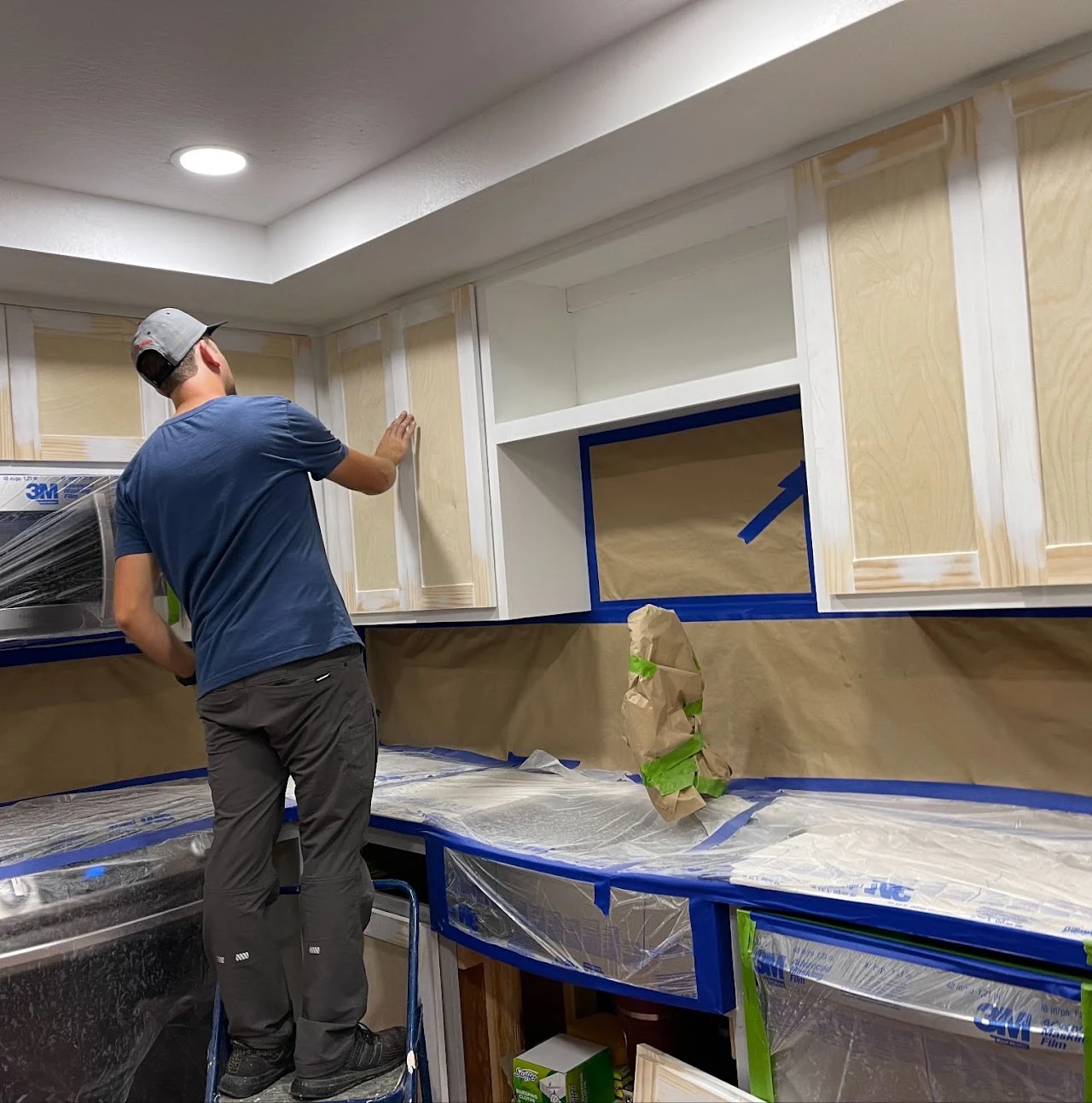 Worker finishing kitchen cabinets with counters and appliances covered for protection
