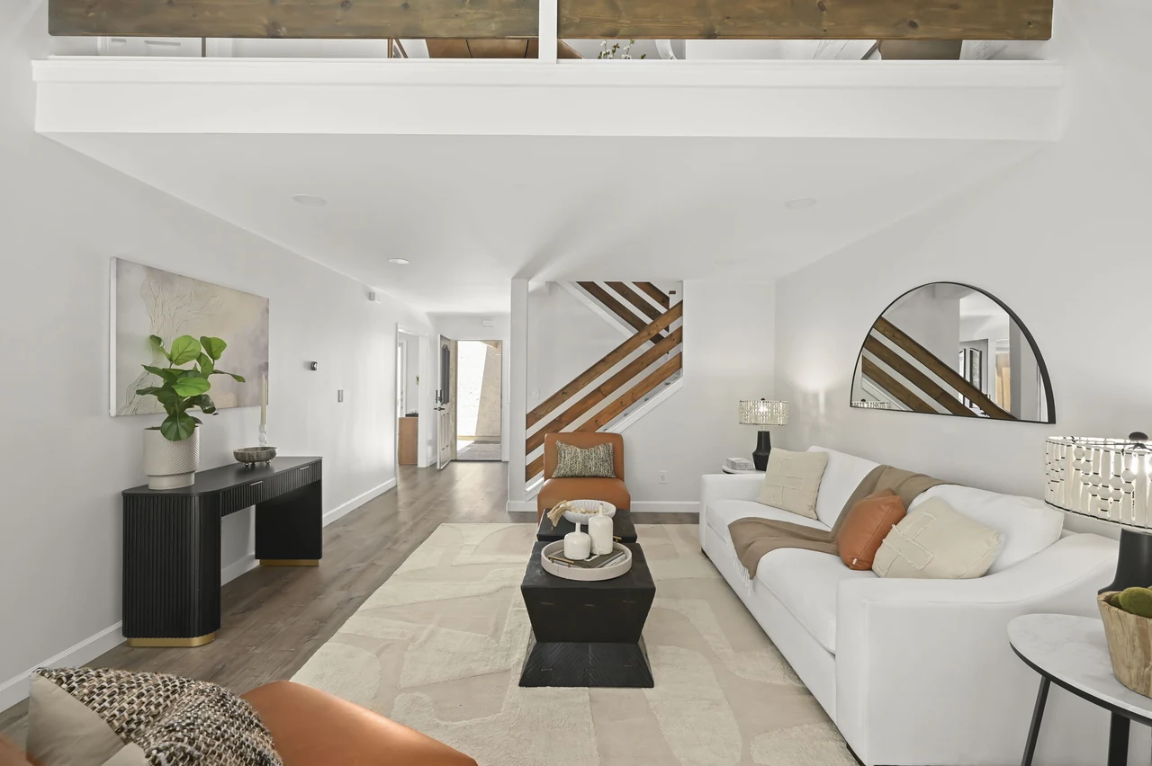 Living room with a sofa, round mirror and view toward the staircase